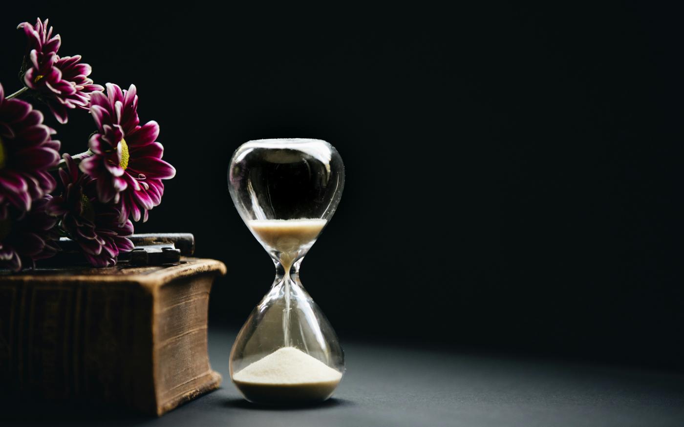 clear hour glass beside pink flowers by Nathan Dumlao courtesy of Unsplash.