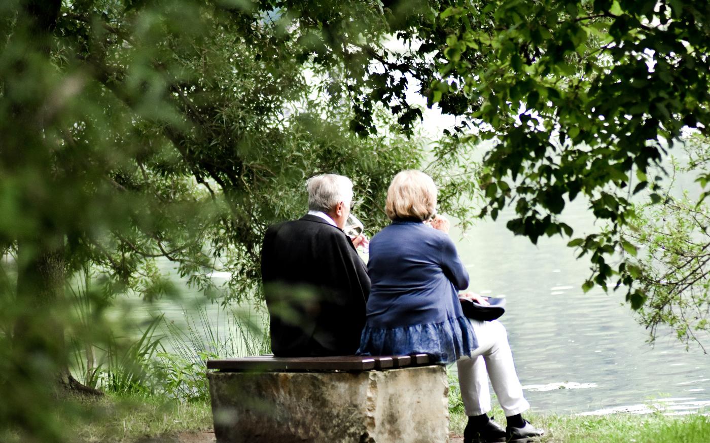 two people sitting on pavement facing on body of water by Sven Mieke courtesy of Unsplash.